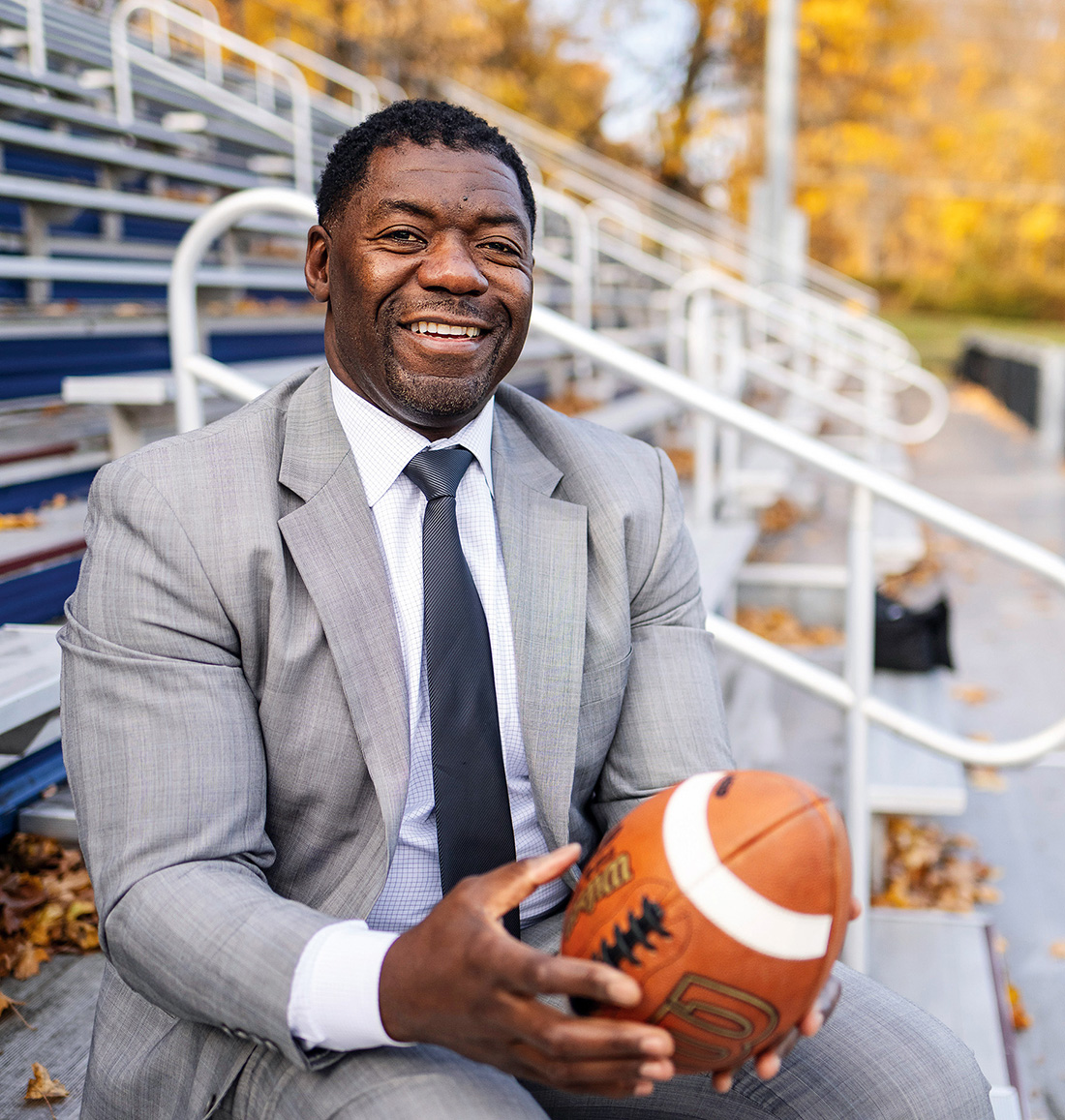 A man sits in the stands on a football field, holding a football in his hands.